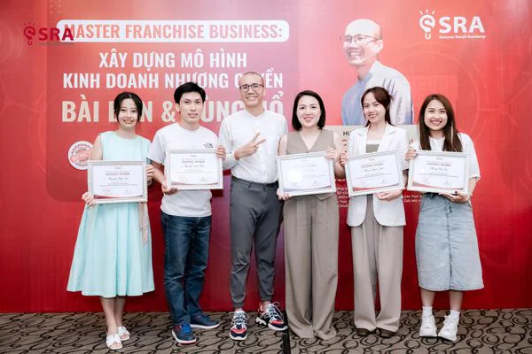 Năm học viên nhận chứng nhận cùng huấn luyện viên trước backdrop Master Franchise Business